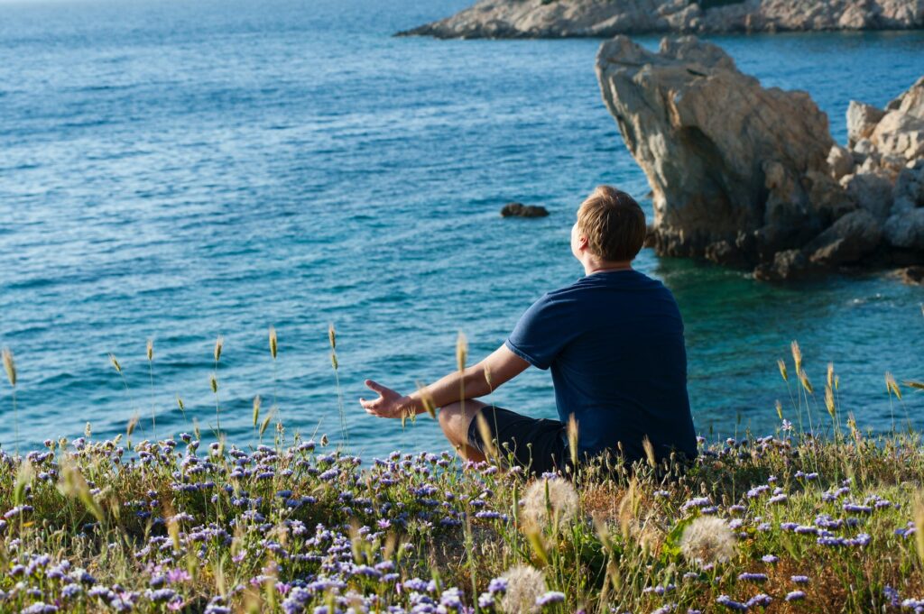 man sitting on flower fields facing ocean